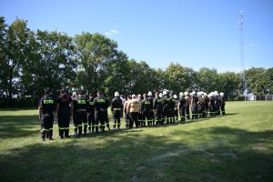 Strażacy OSP ustawieni w szeregu na boisku podczas Gminnych Zawodów Sportowo-Pożarniczych